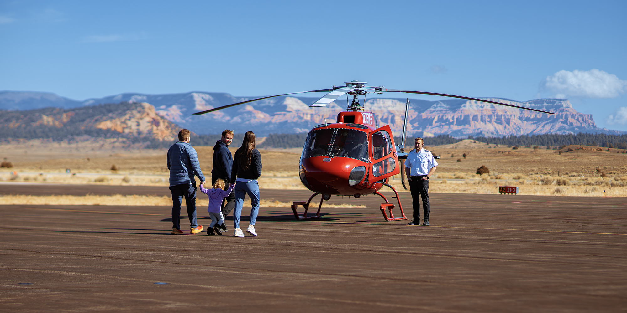 Excited family meets pilot on runway before boarding scenic helicopter tour, stunning Bryce Canyon National Park landscape in background